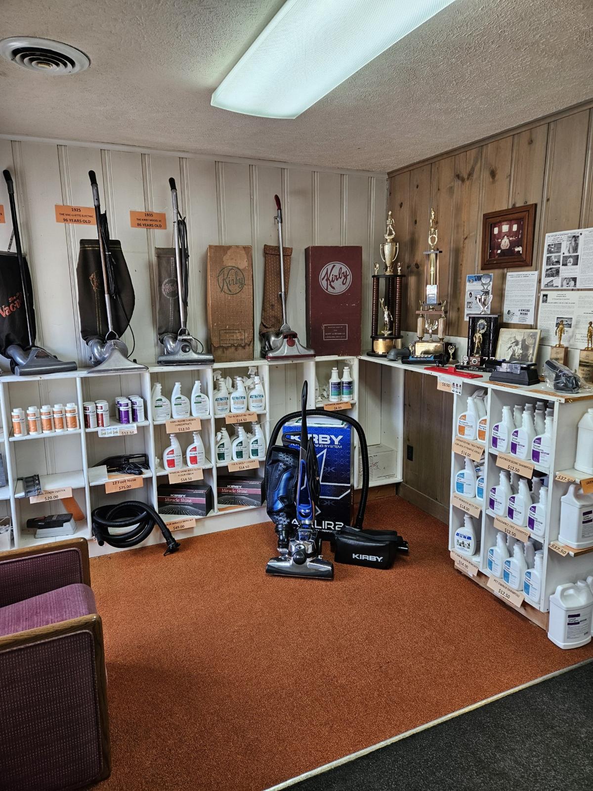 Inside the showroom: vintage Kirby models lined up along the pine-panelled wall, trophies and the new Avalir 2